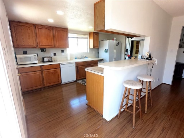 kitchen with kitchen peninsula, white appliances, sink, dark hardwood / wood-style floors, and a breakfast bar area