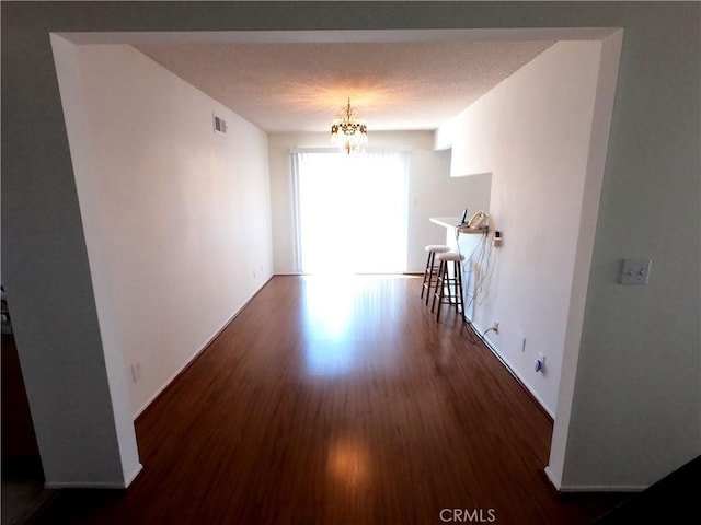 empty room featuring dark hardwood / wood-style flooring, a chandelier, and a textured ceiling