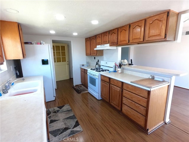 kitchen with kitchen peninsula, dark hardwood / wood-style flooring, white appliances, and sink