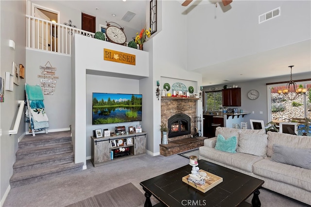 carpeted living room with a stone fireplace, a high ceiling, and ceiling fan with notable chandelier