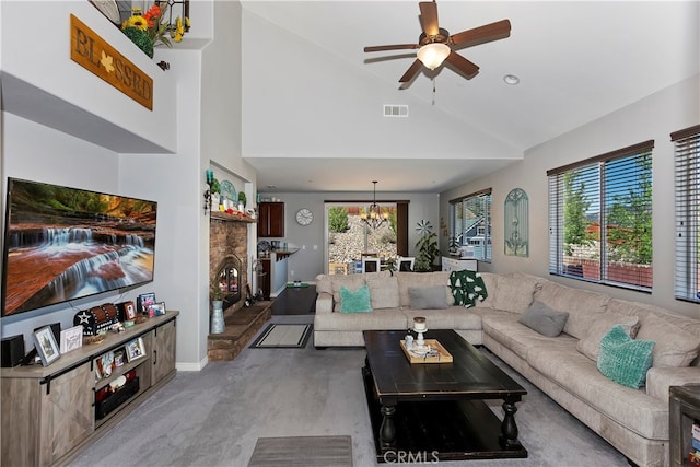 carpeted living room featuring high vaulted ceiling, ceiling fan with notable chandelier, and a stone fireplace