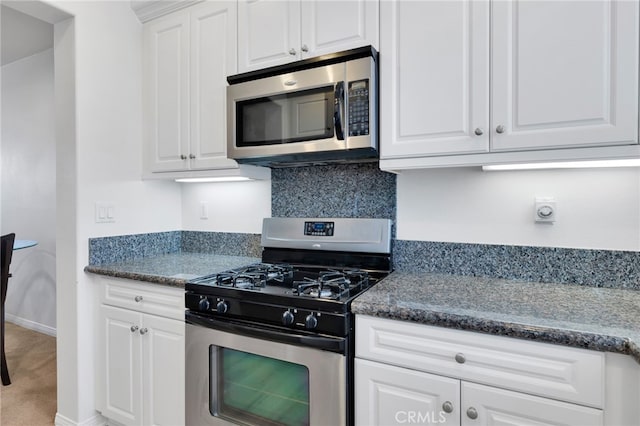 kitchen with appliances with stainless steel finishes, dark stone countertops, and white cabinetry