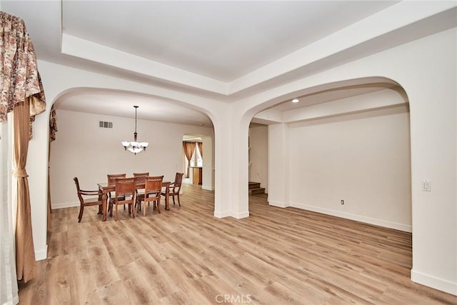 dining room with a chandelier, light hardwood / wood-style floors, and a raised ceiling