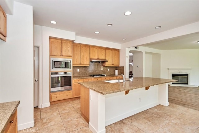 kitchen featuring backsplash, a kitchen island with sink, sink, a kitchen bar, and stainless steel appliances