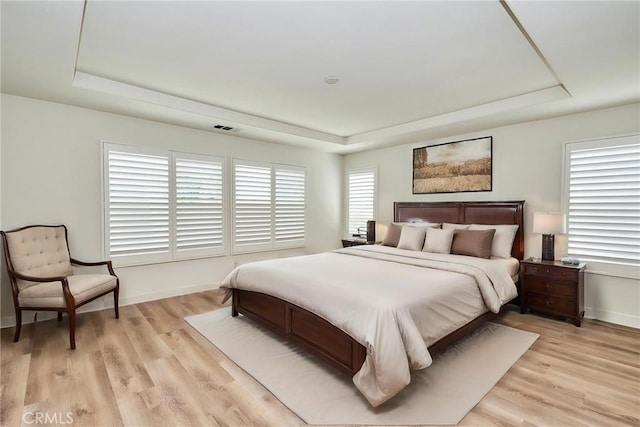 bedroom with a raised ceiling, light wood-type flooring, and multiple windows