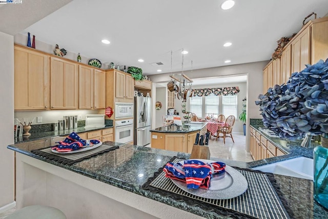 kitchen with dark stone counters, white appliances, light brown cabinetry, and kitchen peninsula