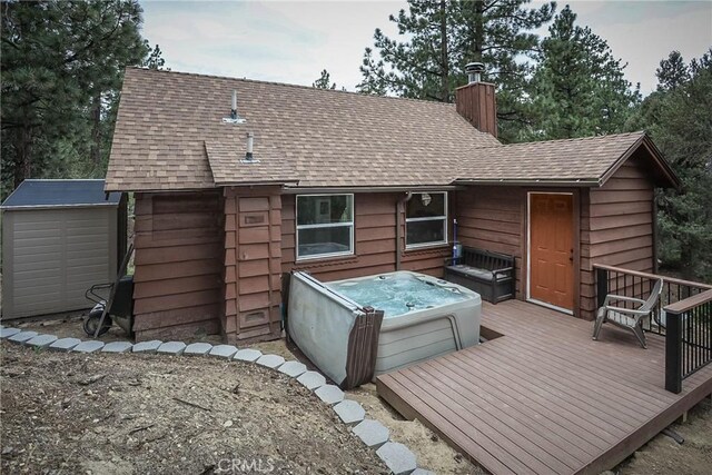 rear view of property with a storage shed, a wooden deck, and a hot tub