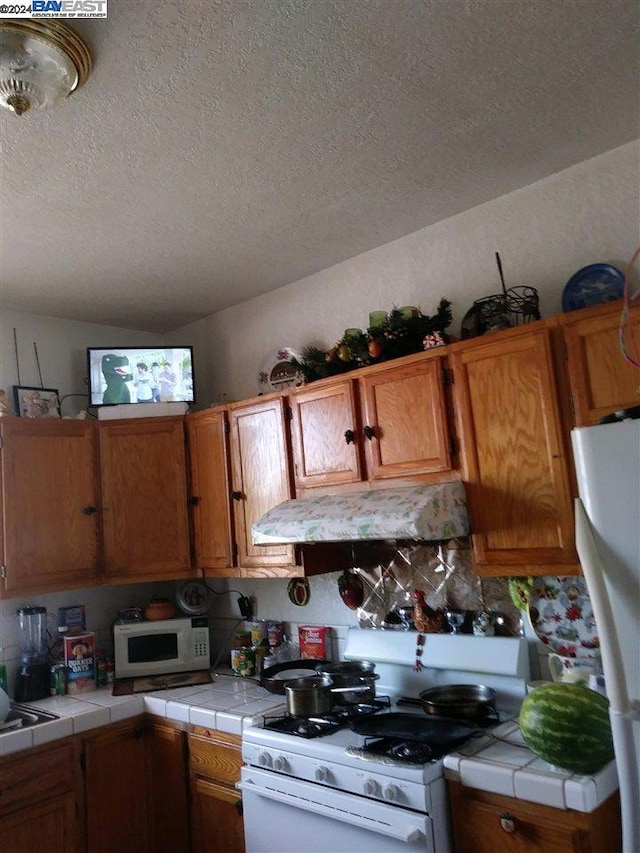 kitchen featuring tile countertops, white appliances, and a textured ceiling