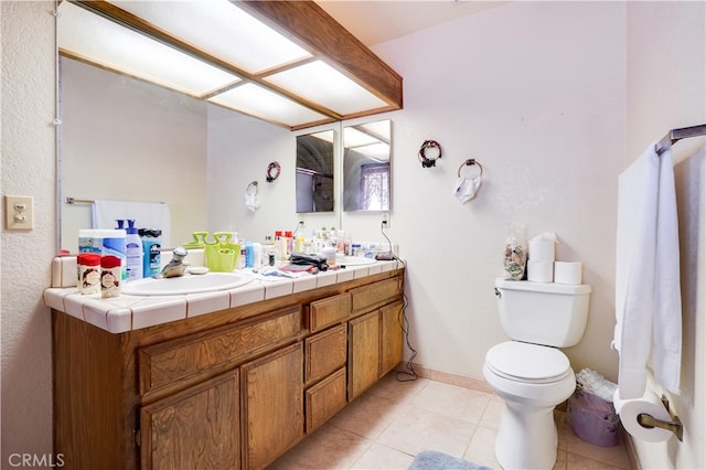 bathroom with toilet, a sink, baseboards, tile patterned floors, and double vanity