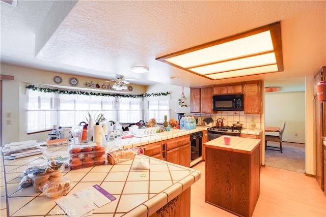 kitchen with brown cabinets, tile counters, stainless steel stove, a kitchen island, and black microwave