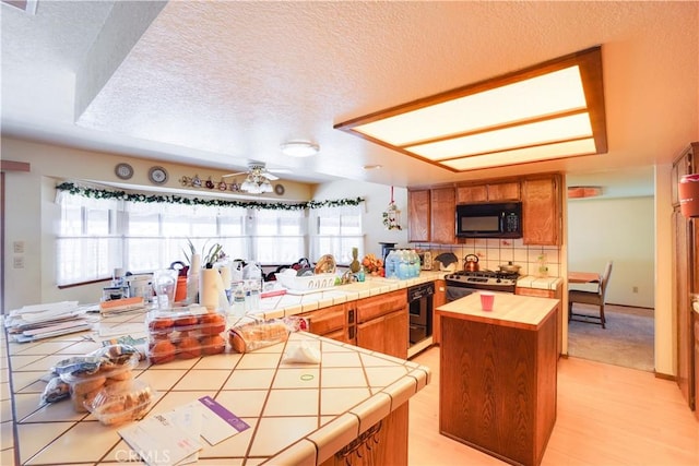 kitchen with black microwave, tile countertops, brown cabinets, and a textured ceiling