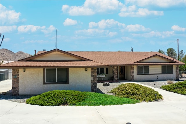 ranch-style house with stone siding, a shingled roof, and stucco siding