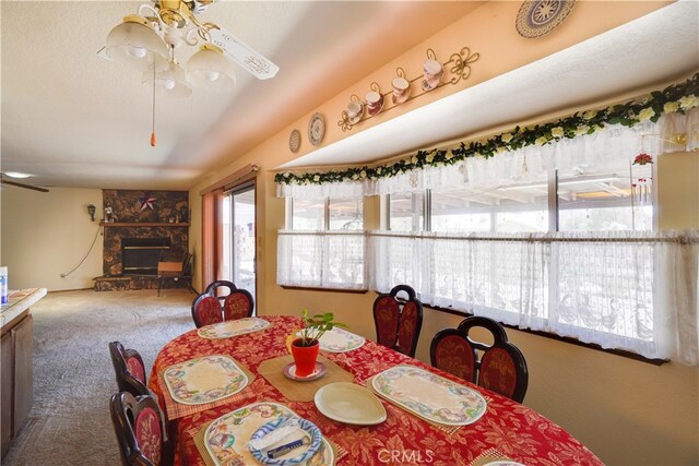 carpeted dining space featuring a textured ceiling, a ceiling fan, and a stone fireplace