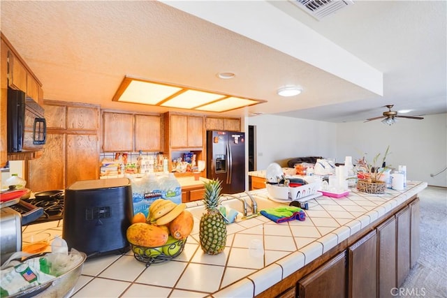 kitchen with light colored carpet, tile countertops, a ceiling fan, visible vents, and black appliances