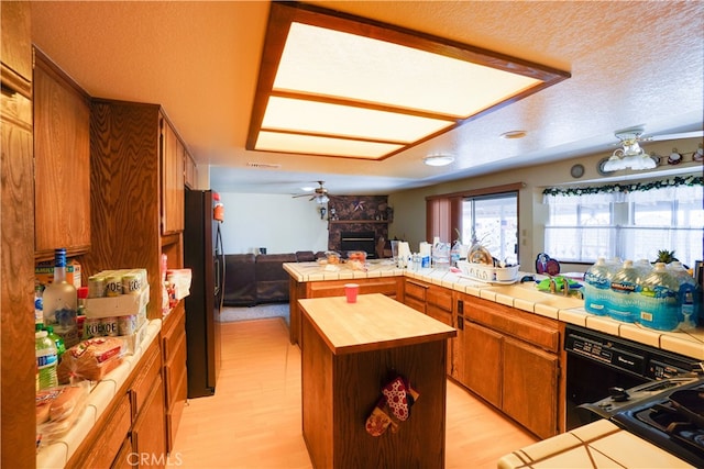 kitchen featuring tile countertops, stainless steel refrigerator with ice dispenser, a fireplace, and a kitchen island