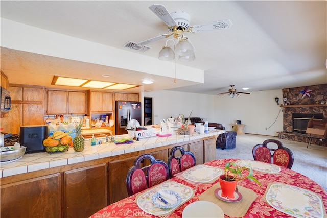 kitchen with tile countertops, ceiling fan, light carpet, stainless steel refrigerator with ice dispenser, and brown cabinetry