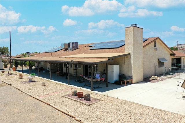 rear view of house featuring a patio, a chimney, fence, roof mounted solar panels, and stucco siding