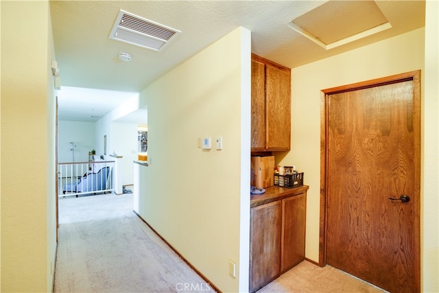 corridor featuring attic access, an upstairs landing, visible vents, and light colored carpet