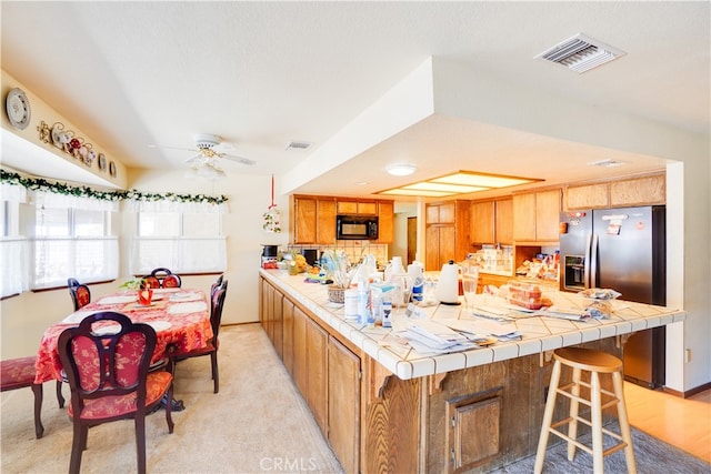 kitchen featuring tile countertops, black microwave, visible vents, and brown cabinets