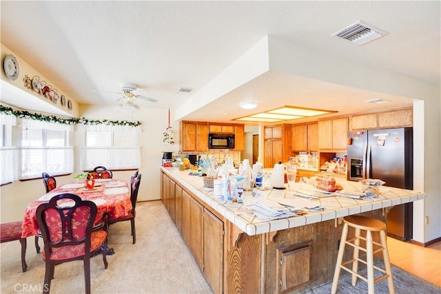 kitchen featuring visible vents, a peninsula, black microwave, stainless steel refrigerator with ice dispenser, and tile counters