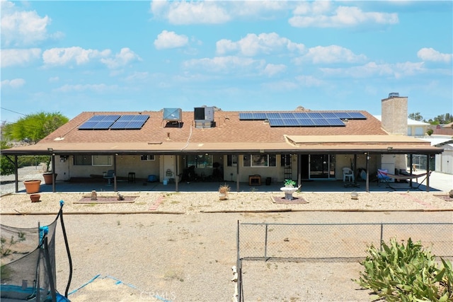 rear view of property with roof mounted solar panels, a patio area, and fence