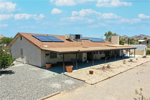 back of house with roof with shingles, a chimney, stucco siding, a patio area, and a mountain view