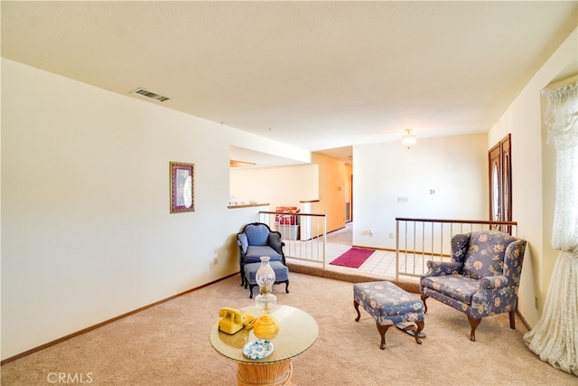 living area with baseboards, an upstairs landing, visible vents, and light colored carpet