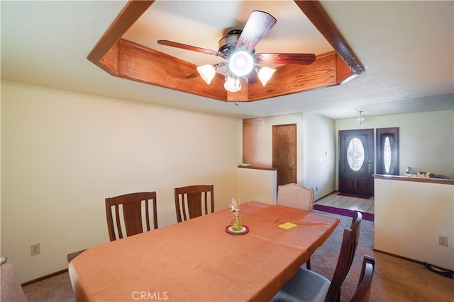 dining room with light carpet, ceiling fan, a raised ceiling, and baseboards