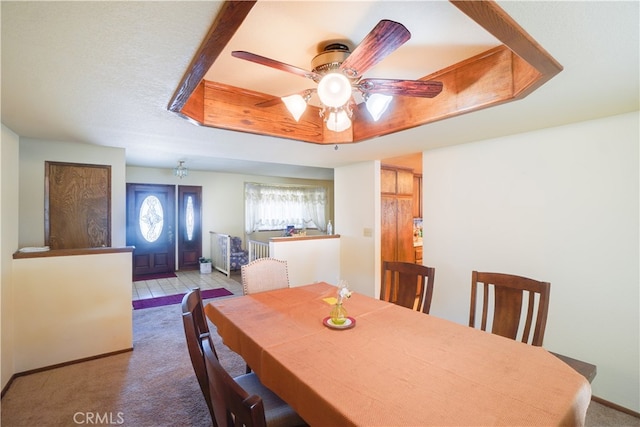 dining room with a raised ceiling, a ceiling fan, and light colored carpet