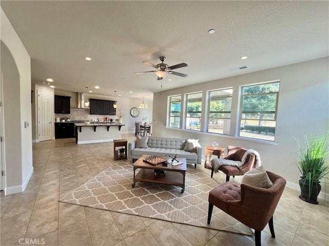 tiled living room with ceiling fan with notable chandelier