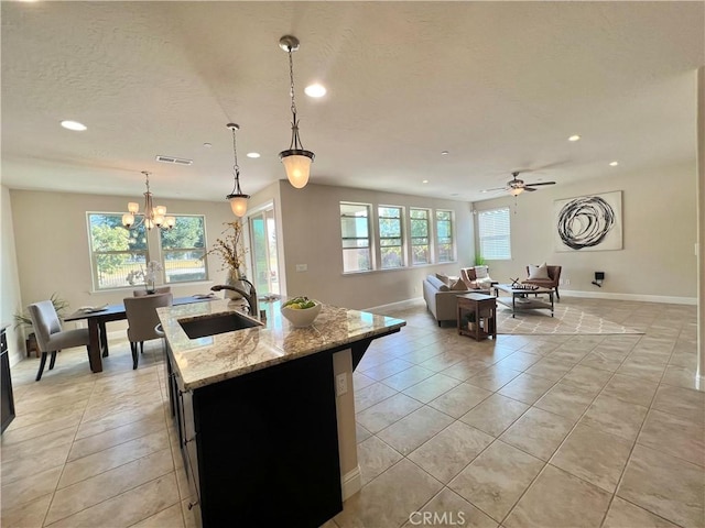 kitchen featuring sink, hanging light fixtures, plenty of natural light, light stone counters, and an island with sink