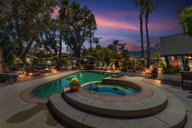 pool at dusk featuring a patio and an in ground hot tub