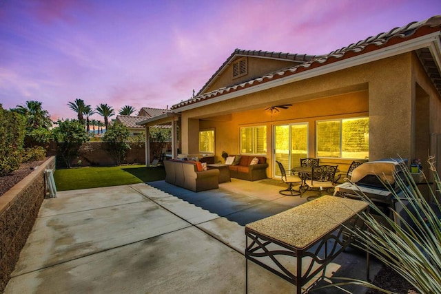 patio terrace at dusk with outdoor lounge area, ceiling fan, and a yard