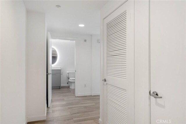 corridor with baseboards, light wood finished floors, and recessed lighting