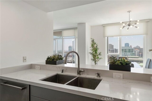 kitchen featuring hanging light fixtures, light stone counters, stainless steel dishwasher, a chandelier, and sink