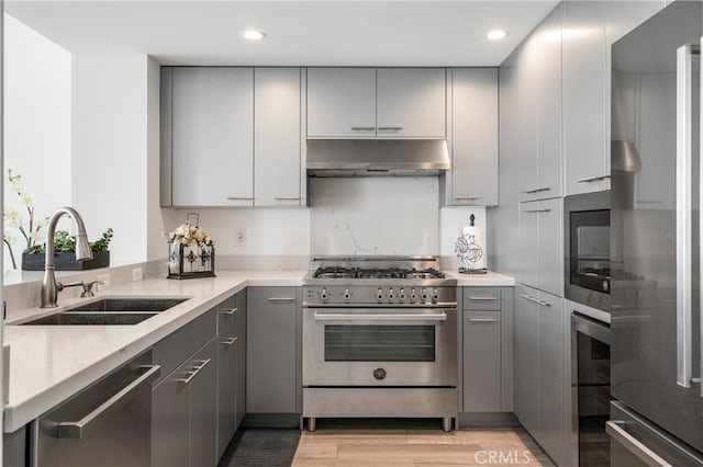 kitchen with light hardwood / wood-style flooring, sink, gray cabinets, appliances with stainless steel finishes, and light stone counters