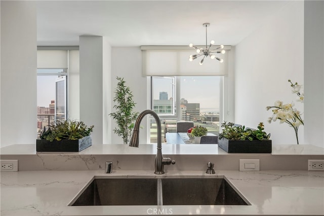 kitchen with light stone counters, a notable chandelier, sink, and pendant lighting