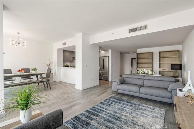 living area featuring baseboards, light wood-style flooring, visible vents, and a chandelier