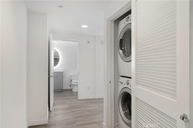 laundry room with light wood-type flooring, recessed lighting, stacked washer / drying machine, baseboards, and laundry area