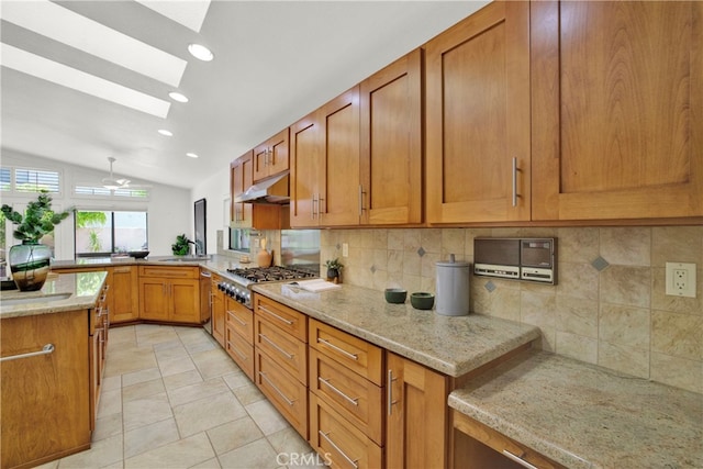 kitchen with tasteful backsplash, light stone countertops, vaulted ceiling with skylight, and stainless steel gas cooktop