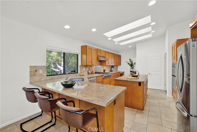 kitchen featuring kitchen peninsula, appliances with stainless steel finishes, a kitchen bar, vaulted ceiling with skylight, and a kitchen island