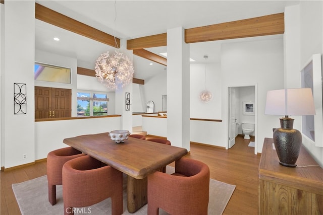 dining space featuring beamed ceiling, hardwood / wood-style floors, a notable chandelier, and a high ceiling