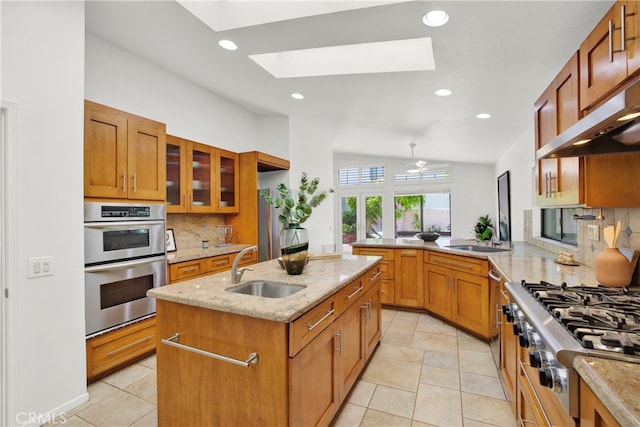 kitchen featuring vaulted ceiling with skylight, backsplash, sink, and an island with sink