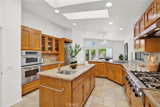 32701 Via Palacio, Rancho Palos Verdes, CA 90275 - kitchen featuring appliances with stainless steel finishes, a skylight, an island with sink, decorative backsplash, and light stone countertops