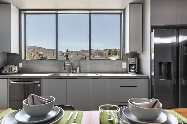 kitchen featuring dishwashing machine, tasteful backsplash, sink, stainless steel fridge, and gray cabinetry