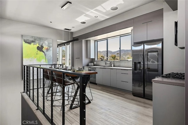 kitchen with gray cabinets, a kitchen bar, a mountain view, light wood-type flooring, and stainless steel fridge with ice dispenser