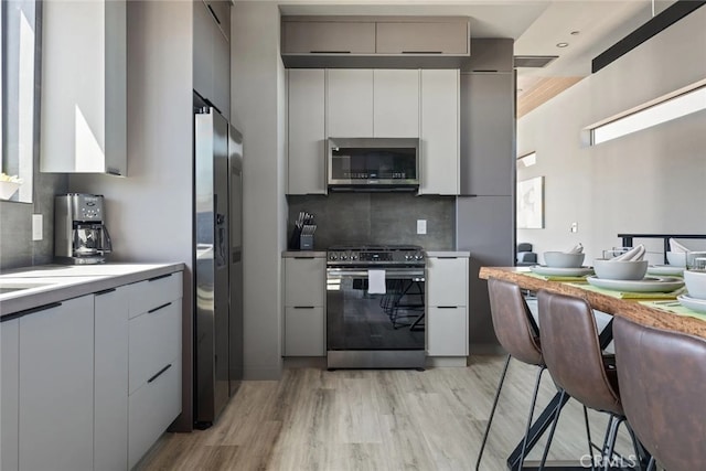 kitchen with decorative backsplash, appliances with stainless steel finishes, gray cabinets, and light hardwood / wood-style flooring