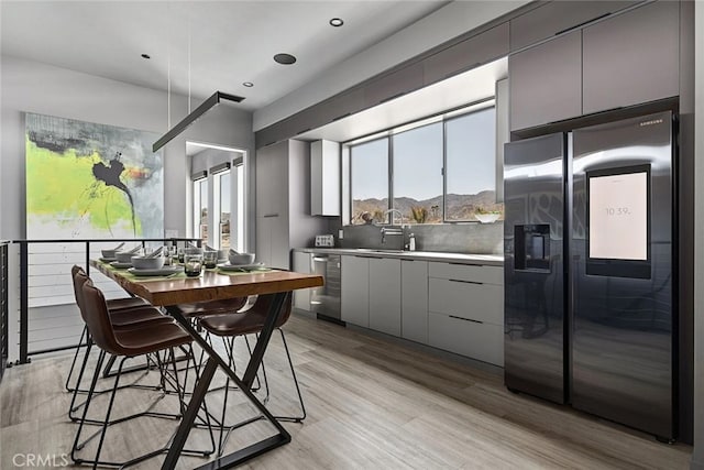 kitchen with stainless steel appliances, gray cabinetry, tasteful backsplash, light hardwood / wood-style flooring, and sink