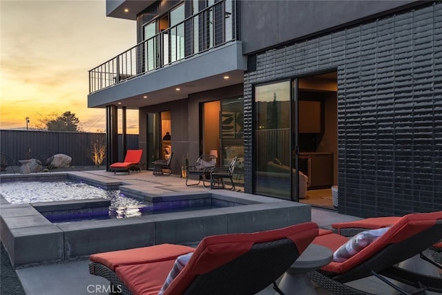 pool at dusk with a patio area and an in ground hot tub