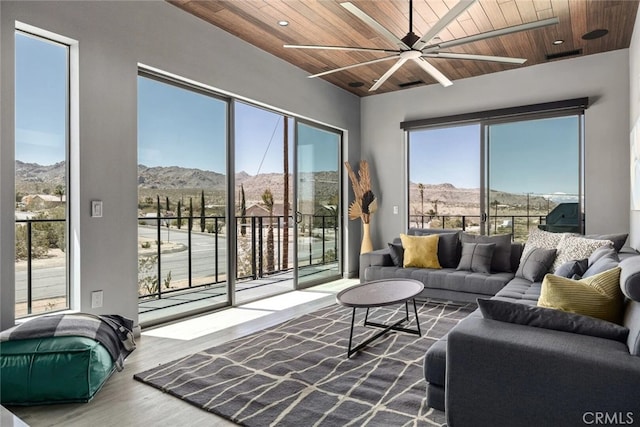 living room with wooden ceiling, a mountain view, plenty of natural light, and ceiling fan